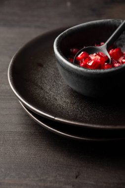 Nar tohumları ve kaşık tabakların üzerinde siyah kâsenin üst görüntüsü ve karanlık masa, dikey, kopyalama alanı ile