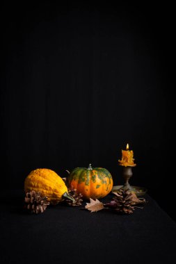 Sonbahar yapraklı balkabaklarının üst görünümü ve yanan mum, masa örtüsü ve siyah arkaplan üzerinde, dikey, kopyalama alanı ile