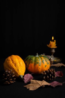 Balkabakları, sonbahar yaprakları ve yanan mum ile hareketsiz yaşamın üst görünümü, seçici odak, masa örtüsü ve siyah arkaplan, dikey, kopyalama alanı ile