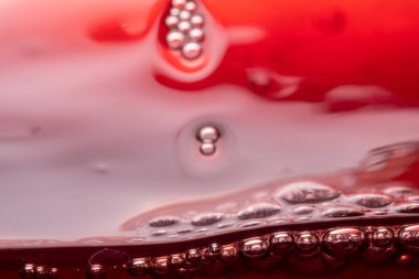 Bardaktaki kırmızı şaraptan damlalar, kabarcıklar ve dalgalar.