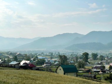 Güneşli bir günde yeşil dağların eteğinde küçük bir kasaba, Altai, Rusya