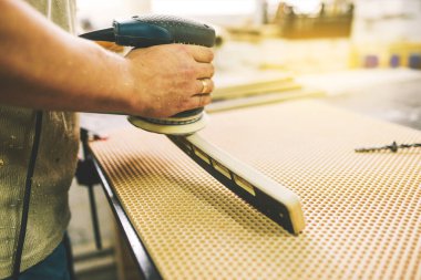 Bir adam ahşap parçayı öğütücüyle işliyor. Marangozluk atölyesinde mobilya imalatı. Ahşap cilası makinesi. Hobi, el işi ve serbest çalışma kavramı.