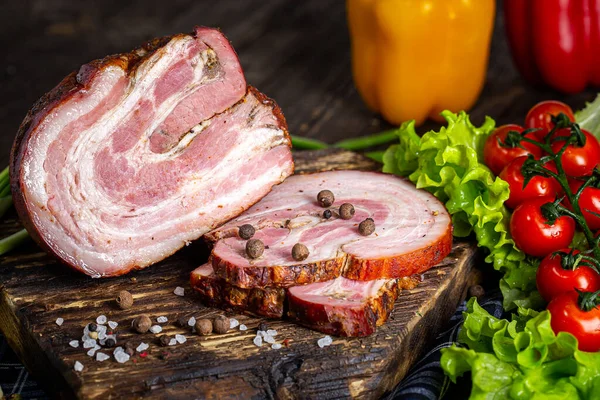 smoked pork meat, spiced bacon, slices, fresh vegetables, herbs and spices, on a black wooden, cutting kitchen board, rustic style dark and moody, black background