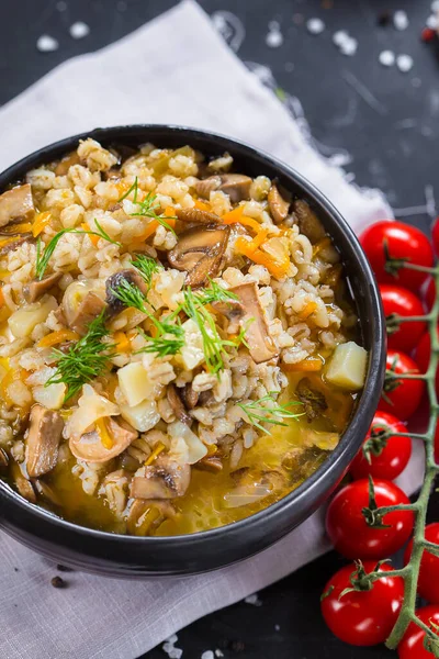 on a plate hot soup with potatoes, mushrooms and barley porridge, cherry tomatoes, cutlery on a black isolated background, top