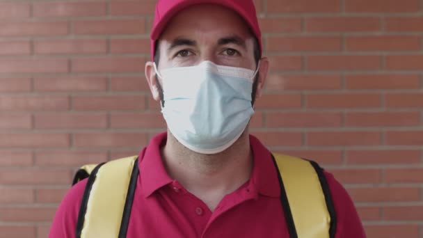 Consegna giovane uomo con cappuccio rosso guardando la fotocamera mentre indossa maschera facciale — Video Stock