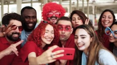 Bir grup çok ırklı taraftar spor hayranı cep telefonuyla selfie çekiyor. 