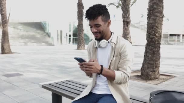 Jeune homme hispanique utilisant un téléphone intelligent à l'extérieur — Video