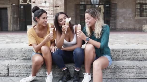 Vielrassige Frauen essen Eis, während sie im Urlaub auf der Straße in der Stadt sitzen — Stockvideo