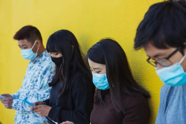 Groep Aziaten met behulp van mobiele telefoon tijdens het dragen van gezichtsmasker — Stockfoto