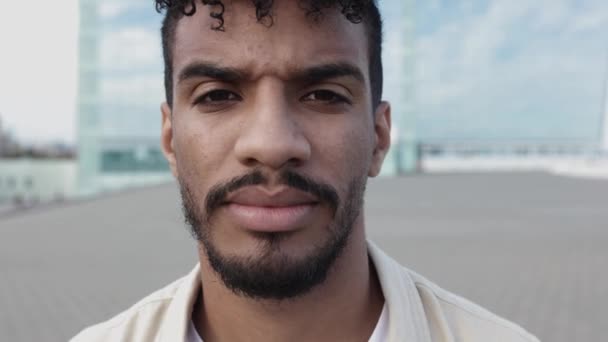 Серйозний молодий латиноамериканський чоловік дивиться на камеру, що стоїть на міській вулиці — стокове відео