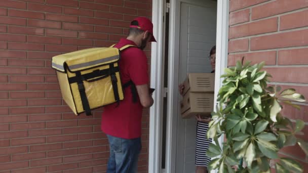 Un mensajero que trae paquetes a una anciana jubilada. Correo hispano en gorra roja y camiseta entregando un paquete a un cliente. Entrega a domicilio, comercio electrónico y concepto de envío — Vídeos de Stock