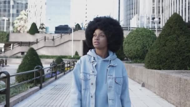 Thoughtful young african woman with afro hairstyle walking in city street — стоковое видео