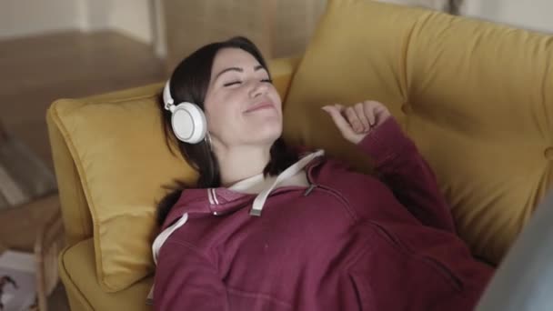 Close up of young happy woman lying on sofa and listening to music — 图库视频影像