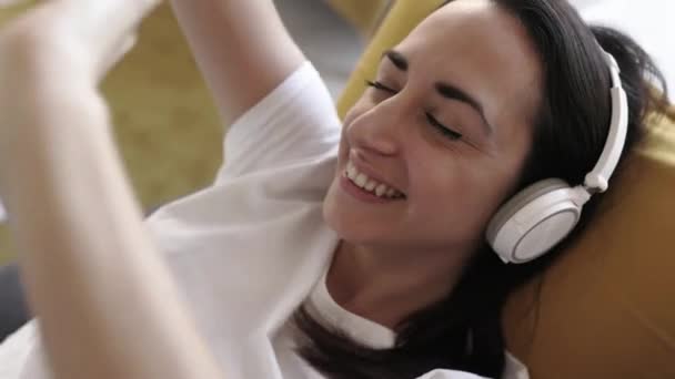 Glad kvinna lyssnar musik när hon sitter på soffan hemma — Stockvideo