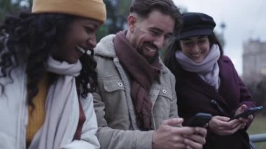 Diverse young people in winter clothes having fun using smart phone outdoors