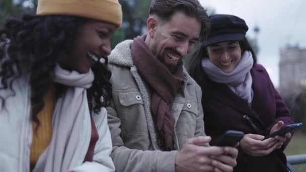 Diverse young people in winter clothes having fun using smart phone outdoors — 图库视频影像