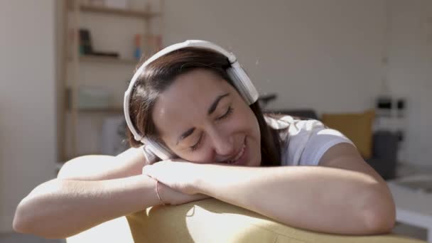 Woman listening to music with headphones at home while sitting on sofa — Vídeo de Stock