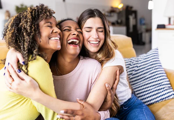 Three happy multiethnic female best friends laughing together at home
