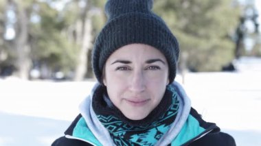 Happy young adult woman in warm clothes in the snow looking at camera