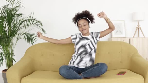 Happy young woman listening to music while dancing sitting on sofa at home