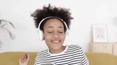 Kanepede dans ederken kulaklıkla müzik dinleyen genç bir kadın. 