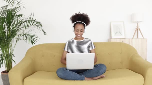 Africano menina americana trabalhando no laptop enquanto sentado no sofá em casa — Vídeo de Stock