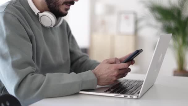 Menutup pertengahan pria dewasa menggunakan ponsel saat bekerja pada laptop di rumah — Stok Video