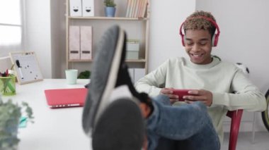 Gülümseyen bağımlı genç Latin adam cep telefonu uygulamasında video oyunları oynuyor.