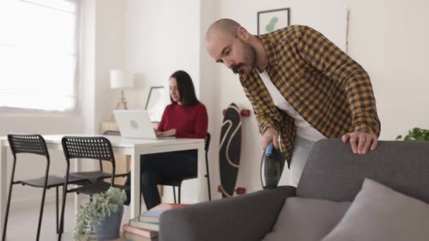 Geconcentreerde hipster jongeman schoonmaken van de bank met een stofzuiger — Stockvideo