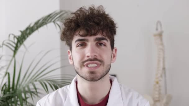 Portret młodego lekarza w gabinecie medycznym uśmiechającego się do kamery — Wideo stockowe