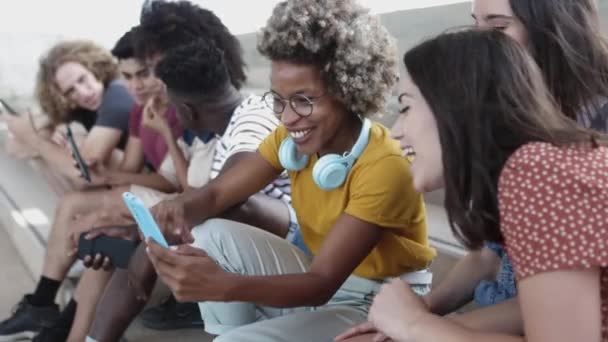 Wielorasowa grupa przyjaciół korzystająca z telefonu komórkowego siedząc na miejskich schodach — Wideo stockowe