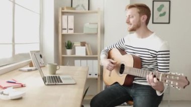 Genç bir adam evde online müzik dersinde gitar çalmayı öğreniyor.