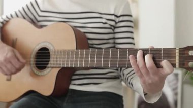 Yakın plan genç adam evde gitar çalıyor.