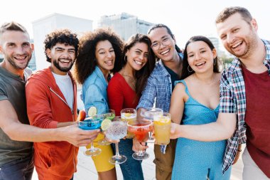Çok ırklı insanlar yaz tatilinde çatıda son moda kokteyllerle kadeh kaldırıyorlar.