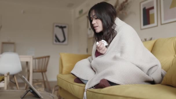 Холодна молода жінка розмовляє з лікарем через відеодзвінок з ноутбуком вдома — стокове відео