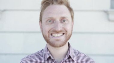 Dışarıdaki kameraya gülümseyen neşeli kızıl saçlı genç adam.