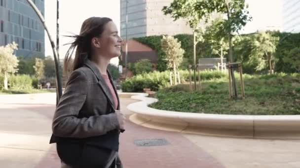 Jovem mulher de negócios sorridente andando ao ar livre na área de edifício de escritório após o trabalho — Vídeo de Stock