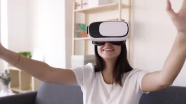 Üç boyutlu gerçeklik kulaklığı kullanarak evde sanal oyunlar oynayan genç bir kadın.