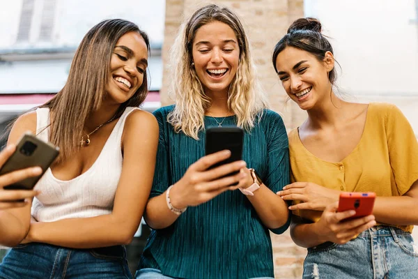 Sonrientes amigas multiétnicas divirtiéndose juntas usando el teléfono móvil — Foto de Stock