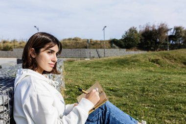 Halk parkında oturan genç İspanyol öğrenci deftere yazı yazıyor.