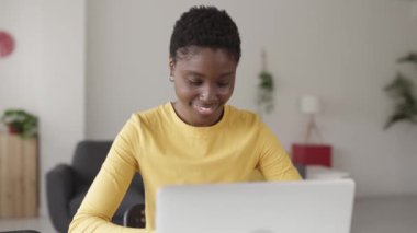 Genç mutlu Afrikalı kadın laptopla evden çalışıyor.