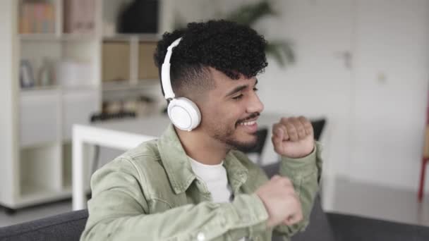 Jovem latino dançando enquanto ouve música com fones de ouvido em casa — Vídeo de Stock