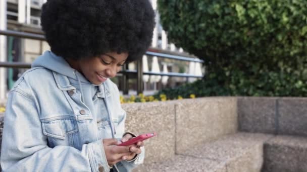 Jong Afrikaans amerikaans vrouw met behulp van mobiele telefoon terwijl zitten buiten — Stockvideo