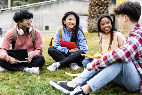 Jóvenes estudiantes sentados en el césped en la universidad del campus —  Fotos de Stock