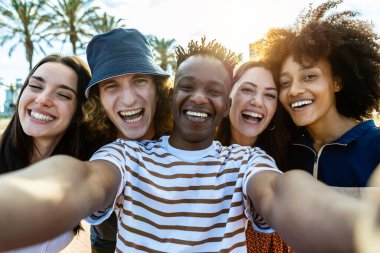 Mutlu bir grup çok ırklı arkadaş dışarıda selfie çekerken eğleniyor.