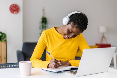 Kulaklıklı, dizüstü bilgisayarla çalışan çok ırklı kız öğrenci.