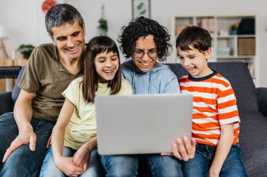 Mutlu bir aile evdeki kanepede yan yana otururken dizüstü bilgisayar kullanıyor..