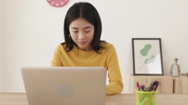 Ev ofisinden laptop kullanan Çinli bir kadın.