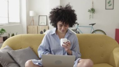 Mutlu Latin Amerikalı kadın evde dinlenirken dizüstü bilgisayar kullanıyor.