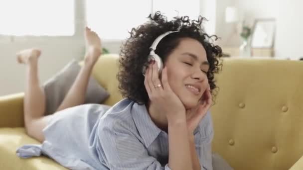 Glad latinamerikansk kvinna avkopplande på soffan lyssna på musik — Stockvideo